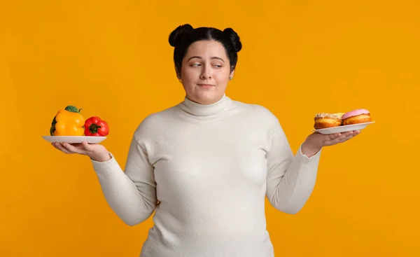 新鮮な野菜とドーナツの2つのプレートの間で選択肥満の女の子 — ストック写真