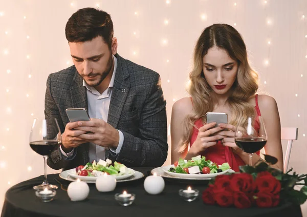 Ζευγάρι ξοδεύουν χρόνο με τα smartphones τους σε ρομαντική ημερομηνία στο εστιατόριο — Φωτογραφία Αρχείου