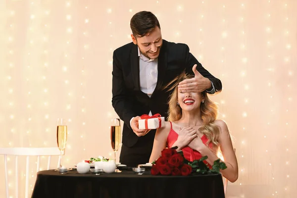 Romantic man surprising his girlfriend with gift on date in restaurant — Stock Photo, Image