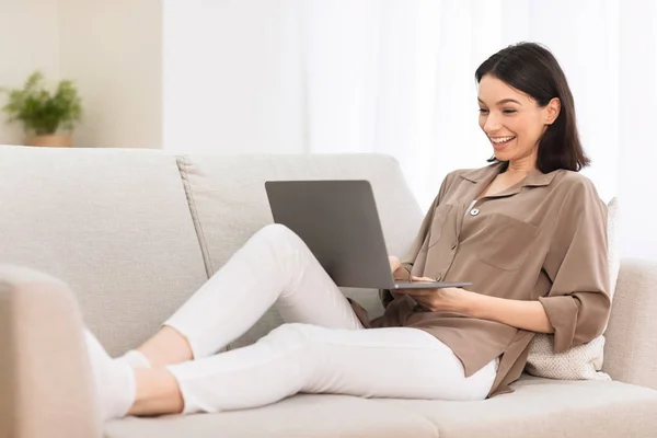 Chica joven que trabaja en el ordenador portátil en línea en el sofá — Foto de Stock