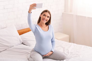 Pregnant Girl With Smartphone Making Selfie On Bed At Home clipart
