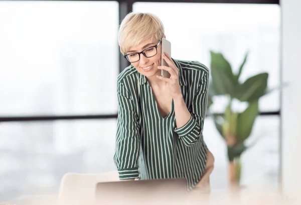 Madura mujer hablando en celular de pie en el lugar de trabajo en la oficina — Foto de Stock