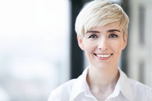 Mujer madura sonriendo de pie contra una ventana interior, retrato —  Fotos de Stock