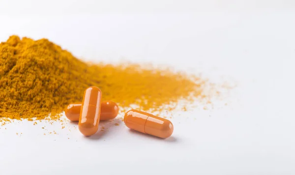 Pile of turmeric capsules and powder on white