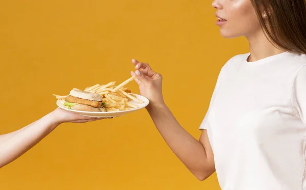 Kadın eli tarafından sunulan tabaktan Fast Food yiyen tanınmayan bir kadın. — Stok fotoğraf