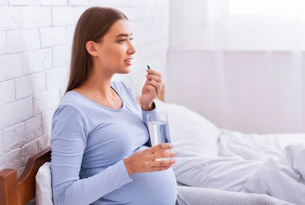 Gravid kvinna som tar medicin piller som håller vatten glas i sängen — Stockfoto