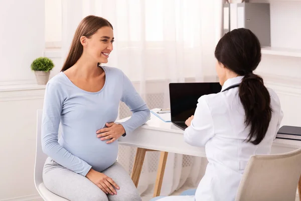 Sorrindo mulher grávida conversando com o médico sentado no escritório moderno — Fotografia de Stock