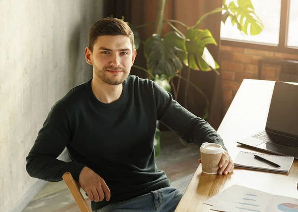 Guy στο Laptop κρατώντας καφέ κάθεται στο γραφείο εργασίας στο γραφείο — Φωτογραφία Αρχείου