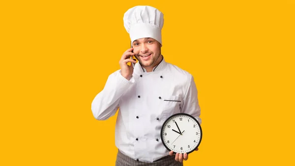 Profissional cozinheiro falando no telefone segurando relógio de pé no estúdio — Fotografia de Stock