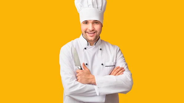 Szakács pózolás holding konyha kés, sárga háttér, panoráma — Stock Fotó