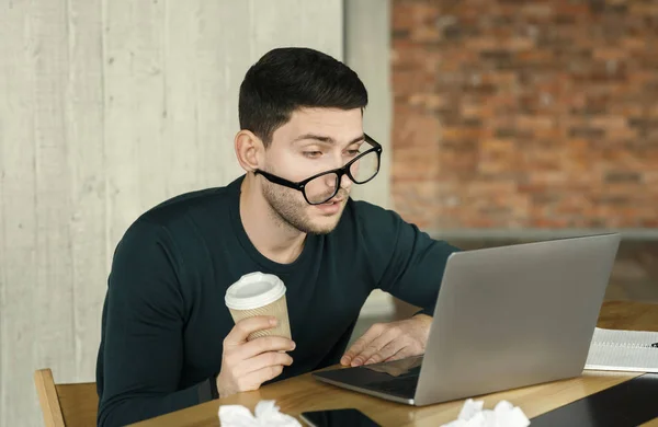 Homem sonolento no laptop segurando xícara de café sentado no escritório — Fotografia de Stock