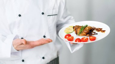 Unrecognizable Chef Holding Plate With Roasted Chicken Standing In Kitchen