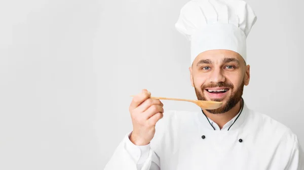 Chef Guy degustación plato celebración cuchara posando sobre fondo gris — Foto de Stock