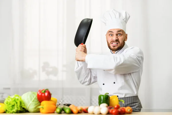Šílený profesionální kuchař chlazení smažení pan šklebící se stojící v kuchyni — Stock fotografie
