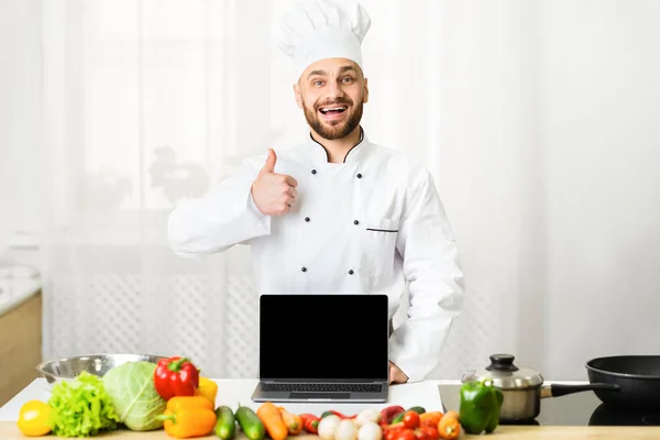 Chef mostrando laptop tela em branco Gesturing Polegares-Up em pé na cozinha — Fotografia de Stock