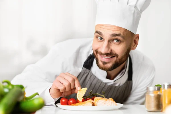 Homem cozinheiro feliz chapeamento de bife de salmão na cozinha restaurante — Fotografia de Stock