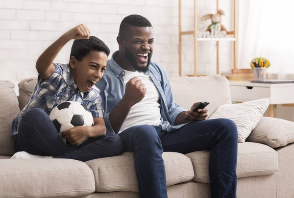 Чёрный отец и сын футбольные фанаты смотрят футбол по телевизору — стоковое фото