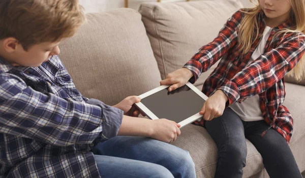 Jaloerse broer en zus trekken apart tablet zitten op de bank — Stockfoto