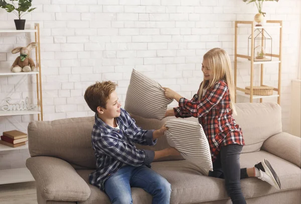 Šťastný bratr a sestra mají polštář boj na gauči uvnitř — Stock fotografie