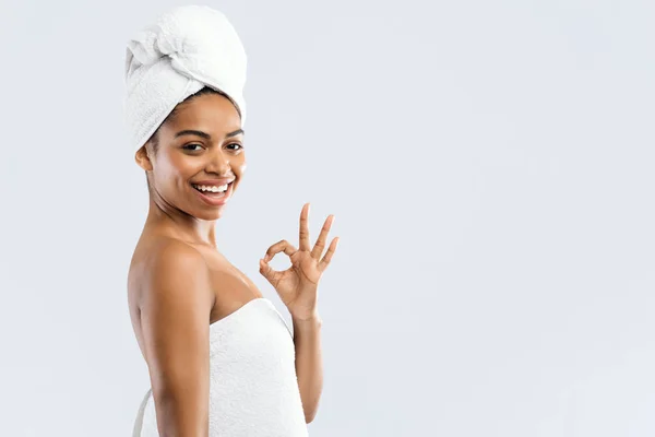 Zufriedenes schwarzes Mädchen in Handtüchern zeigt okay Geste und lächelt — Stockfoto