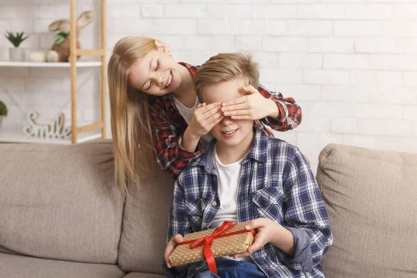 Schwester deckt Brüdern Augen zu und schenkt Geburtstagsgeschenk im Sitzen — Stockfoto