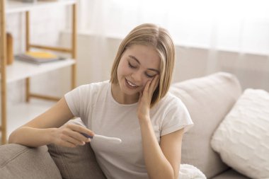 Hamilelik testi tutan mutlu ve şaşırmış genç bir kadın.