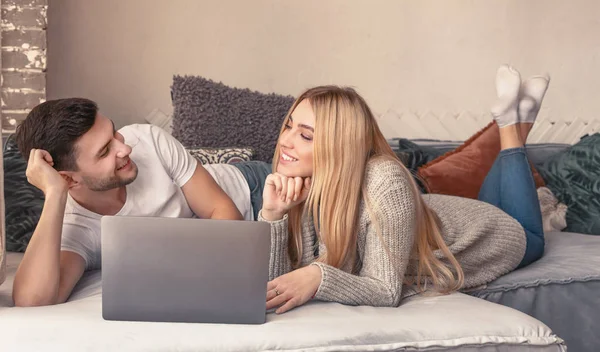 Joven pareja feliz en el sofá discutiendo qué comprar con el ordenador portátil —  Fotos de Stock