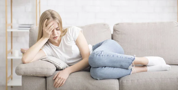 Mujer joven trastornada acostada en el sofá, sufriendo de dolor de cabeza — Foto de Stock