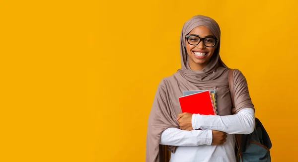 Sonriente afro musulmana estudiante en pañuelo para la cabeza y gafas con cuadernos — Foto de Stock