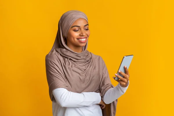 Chica musulmana negra en pañuelo para la cabeza usando teléfono inteligente, mensajes de texto o navegar por Internet — Foto de Stock