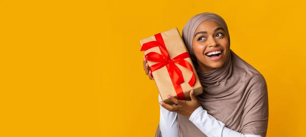 Schwarzes Mädchen im Hijab hält Geschenkbox am Ohr, erraten Geschenk — Stockfoto