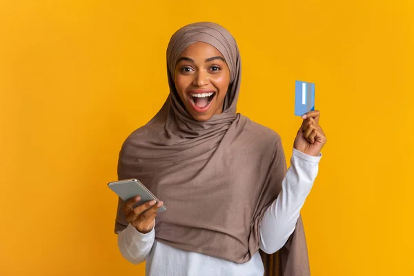 Здорова чорна мусульманська дівчина в Хіджабі тримає кредитну картку та смартфон — стокове фото