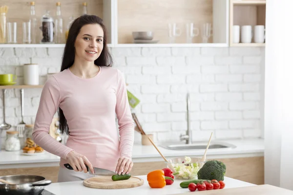 Ung kvinna skär färska grönsaker i köket — Stockfoto