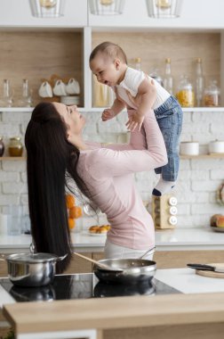 Anne oğlunu havaya kaldırıyor, birlikte öğle yemeği pişiriyor.