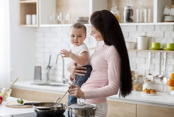 Glückliches Baby hilft Mama beim Kochen von Mittagessen in der Küche — Stockfoto