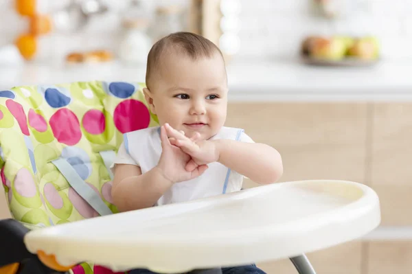 Счастливый ребенок хлопает в ладоши, сидя в стульчике на кухне — стоковое фото