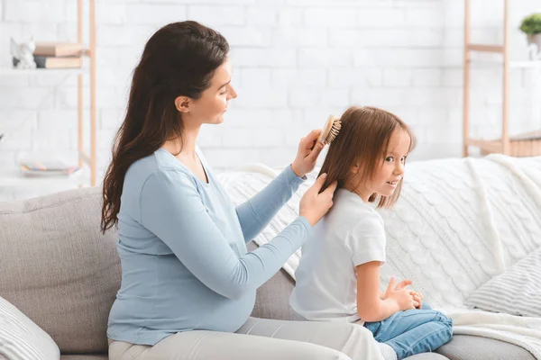 Houden van zwangere vrouw kammen haar kleine dochter haar — Stockfoto