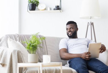 Portatif bilgisayarı olan neşeli Afrikalı adam yan bakıyor.