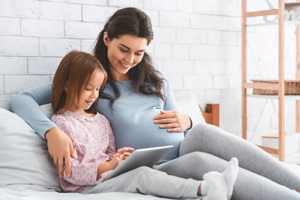 Hamile anne ve küçük kızı pijamalarıyla dijital tablet kullanıyorlar. — Stok fotoğraf