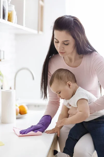 Moeder met baby schoonmaak keuken tafelblad, vrije ruimte — Stockfoto