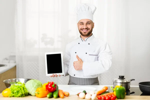 Chef uomo mostrando schermo Tablet gesticolando Pollici in piedi in cucina — Foto Stock