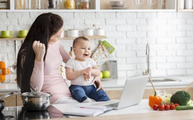 Başarılı olan olumlu kadın, bebekle birlikte dizüstü bilgisayarda çalışıyor.