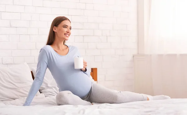 孕妇抱着咖啡杯坐在床上 — 图库照片
