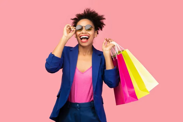 Aufgeregte schwarze Frau mit Einkaufstaschen im rosa Studio — Stockfoto