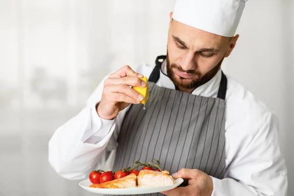 Chef masculino espremendo limão chapeamento assado salmão bife na cozinha — Fotografia de Stock