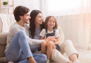 Sevgi dolu ebeveynler küçük kızlarını gıdıklıyor, evde birlikte eğleniyorlar..