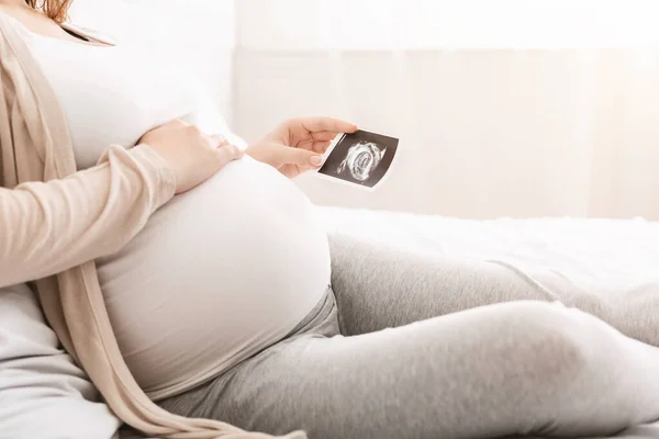 Mujer embarazada tocando el vientre y mirando la ecografía —  Fotos de Stock