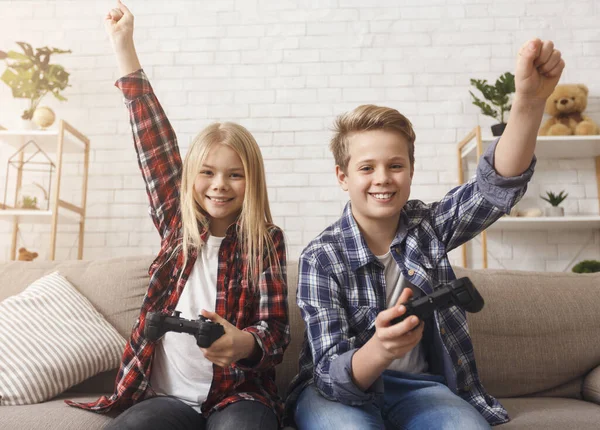 Niños jugando videojuegos juntos celebrando la victoria sentados en el sofá — Foto de Stock