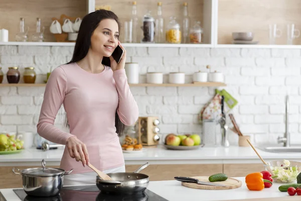 Young woman talking on phone and cooking lunch at kitchen — 스톡 사진