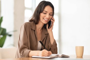 Gülümseyen menajerin portresi telefon görüşmesi yapıyor ve yazıyor.